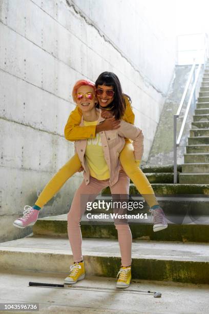 two alternative friends having fun, wearing yellow and pink jeans clothes - piggyback stock pictures, royalty-free photos & images