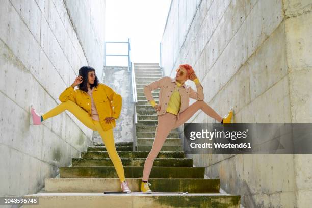 two alternative friends posing on steps, wearing yellow and pink jeans clothes - fashion stock-fotos und bilder