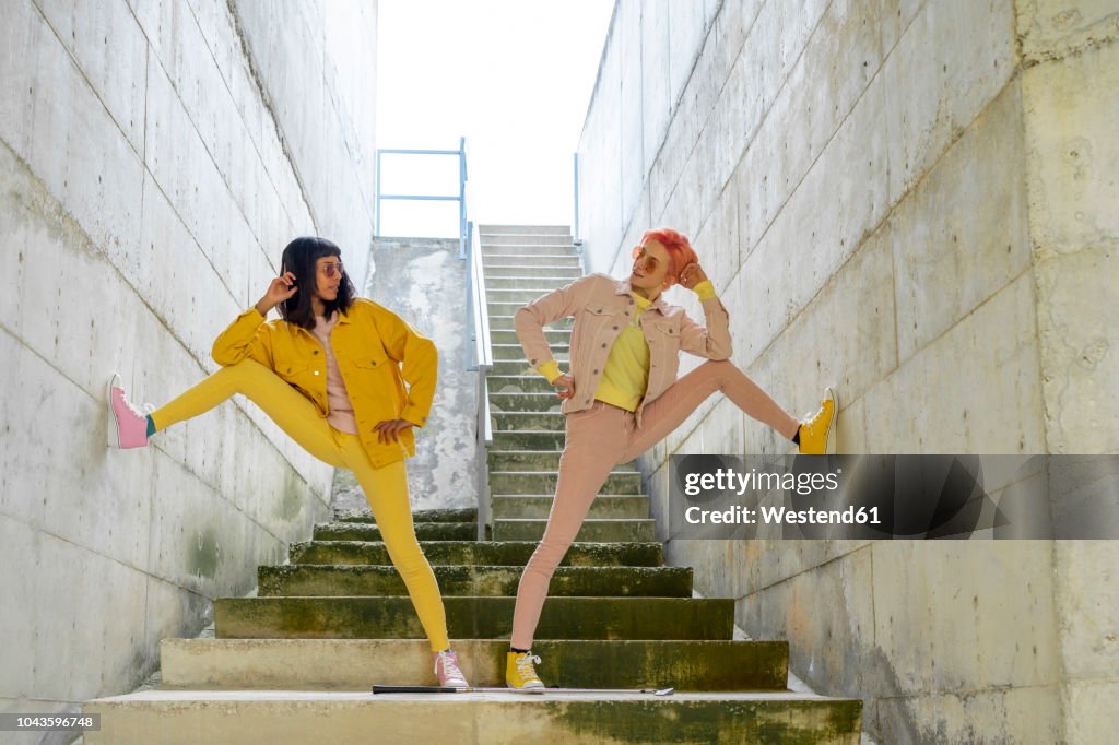 Two alternative friends posing on steps, wearing yellow and pink jeans clothes