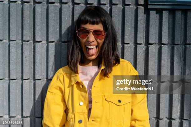portrait of young woman, wearing yellow jeans jacket - mettere fuori la lingua foto e immagini stock
