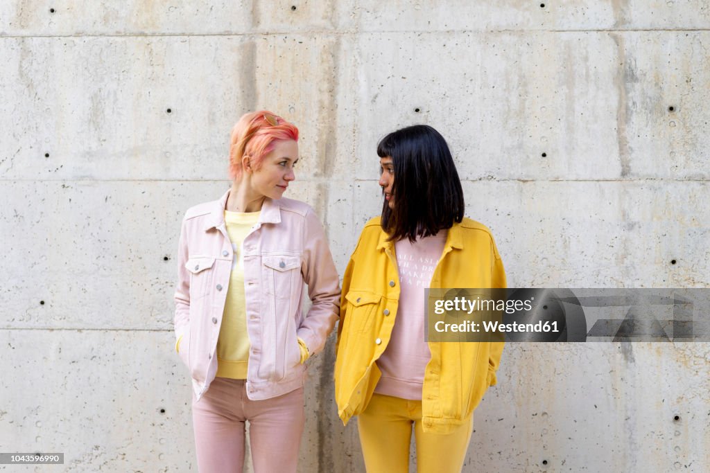 Two alternative friends having fun, wearing yellow and pink jeans clothes, face to face