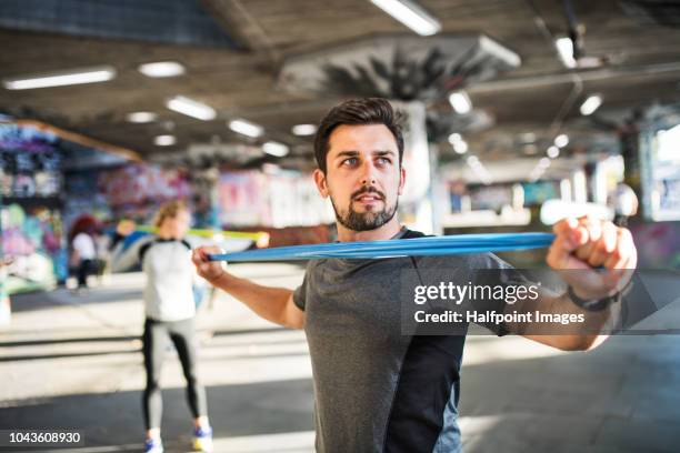 young sporty man exercising with resistance elastic bands under the bridge outside in a city. - elastiekje stockfoto's en -beelden
