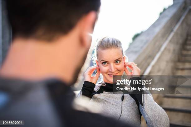 young sporty woman with earphones and unrecognizable man outside in a city, using smart watch. - england slovakia stock pictures, royalty-free photos & images