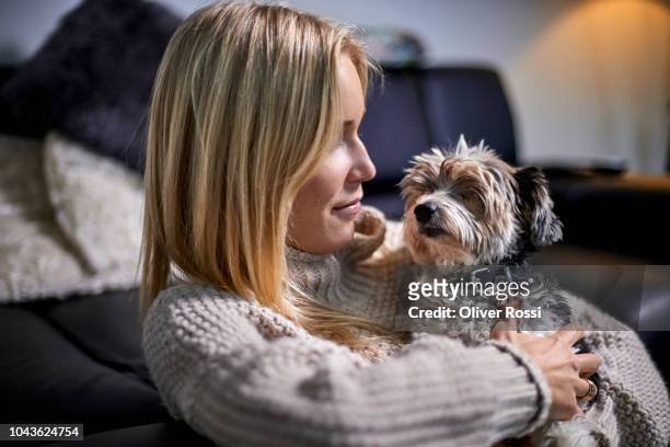 young woman cuddling with lap dog at home - terrier du yorkshire photos et images de collection
