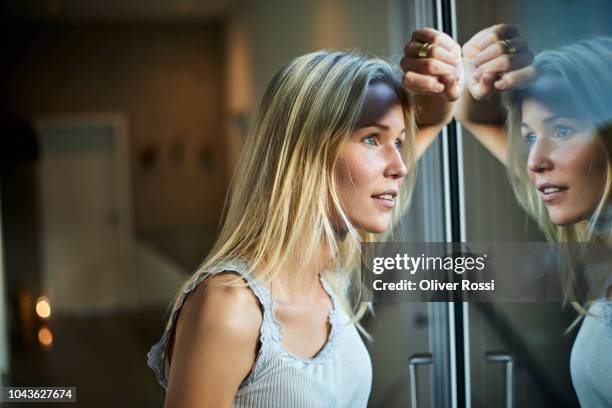 blond young woman looking out of window - desiderio foto e immagini stock