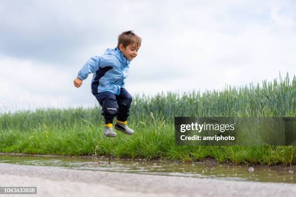 kleiner junge in wasser pfütze springen - kid jumping stock-fotos und bilder