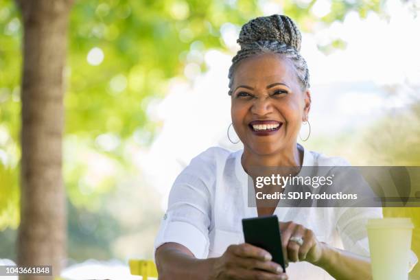 beautiful senior woman uses smartphone outdoors - roll call cup stock pictures, royalty-free photos & images