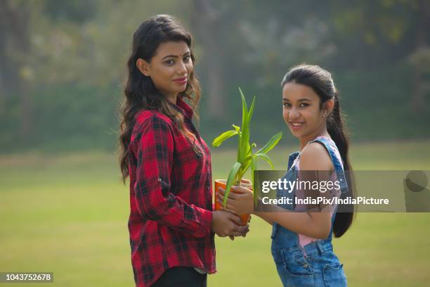 smiling young girl giving a plant in a flower pot to her mother outdoors. - pot plant gift stock pictures, royalty-free photos & images