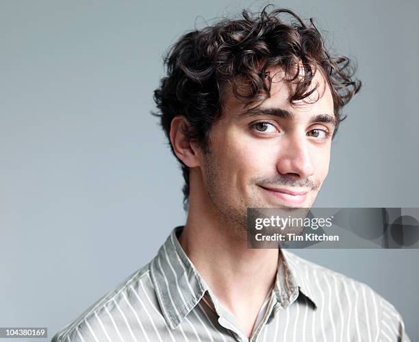 curly-haired dimply-cheeked man smiling, portrait - junger mann allein stock-fotos und bilder