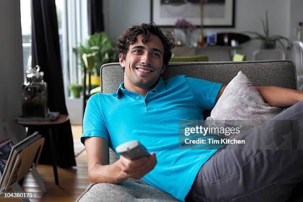 man in living room with remote control, smiling - man living room stockfoto's en -beelden