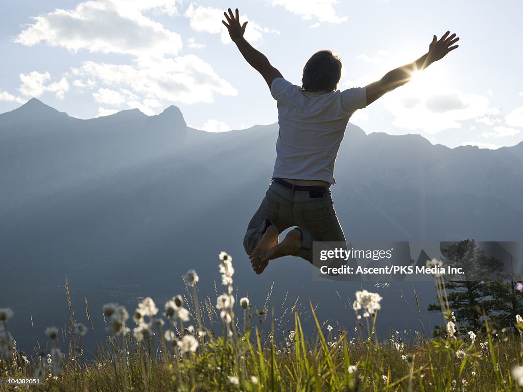 Man leaps for joy in mountain meadow, sunset