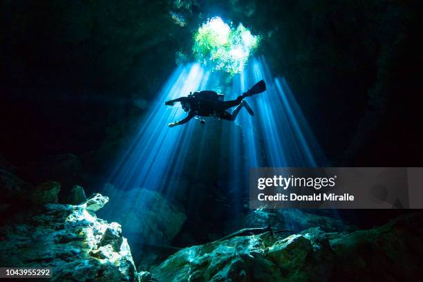 Scuba diver swims through rays of light coming into a massive underground, underwater cave in the Cenote Taj Maha in Quintana Roo, Mexico on...