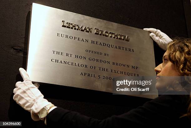 An employee of Christie's auction house adjusts a commemorative plaque from the opening of the Lehman Brothers offices in Canary Wharf, which is...