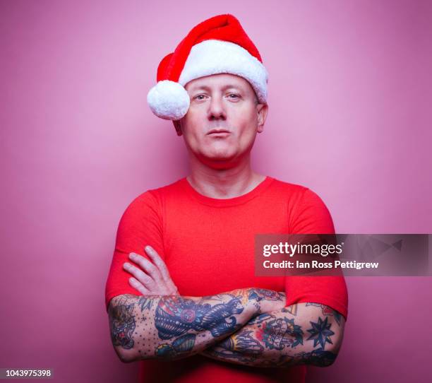 tattooed man wearing santa claus hat - santa hat fotografías e imágenes de stock
