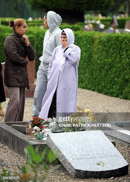 Veiled woman surrounded by members of her family, stands in front of a damaged gravestone in a cemetery where the Muslim section was desecrated by...