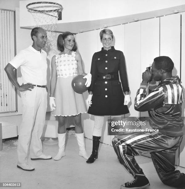 The fashion designer Andre COURREGES posed with two of his models : one wears a short, yellow and white cotton dress, the other a blue wool coat with...