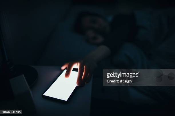 woman reaching and switching off disturbing calls from work on smartphone while sleeping at midnight - resonar fotografías e imágenes de stock