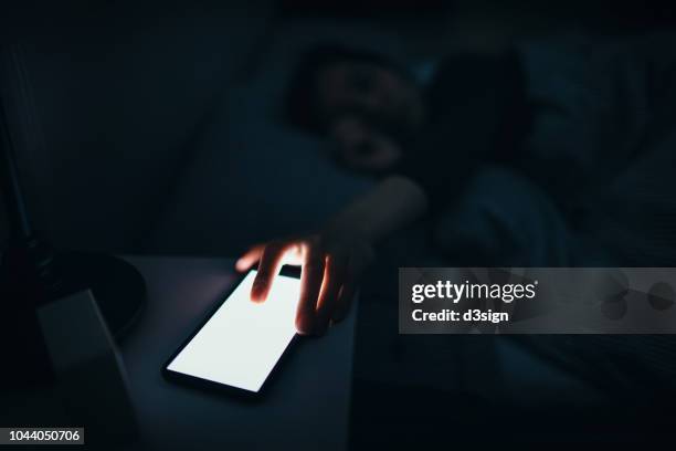 woman reaching and switching off disturbing calls from work on smartphone while sleeping at midnight - soar - fotografias e filmes do acervo