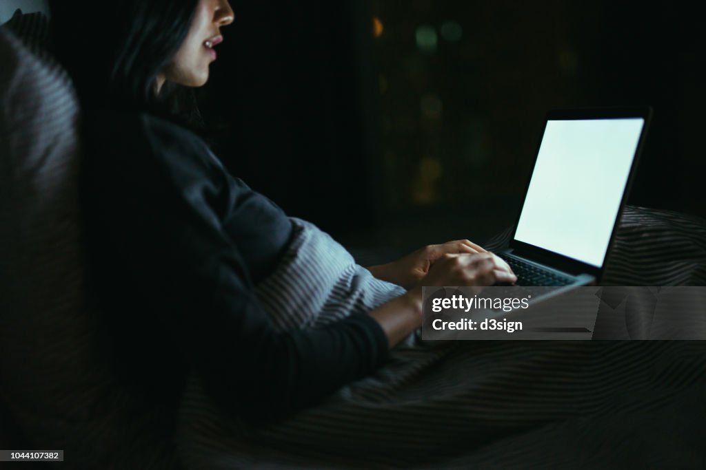 Young Asian woman lying on bed using laptop at night