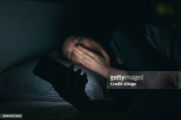 tired woman yawning while using mobile phone on bed at night - woman taking a nap stock-fotos und bilder