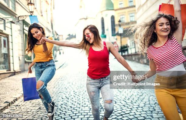 three cheerful female teenager friends with shopping bags walking on the street, jumping. - slovakia city stock pictures, royalty-free photos & images