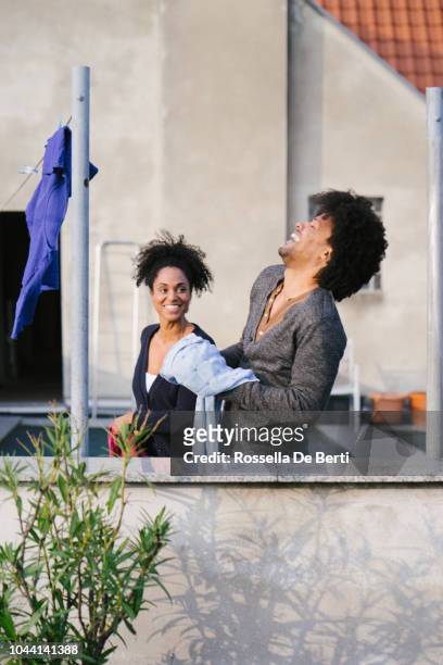 young beautiful couple hanging up laundry on rooftop terrace - afro man washing stock pictures, royalty-free photos & images
