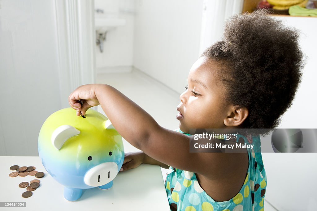 Toddler girl putting pennies in a piggy bank.