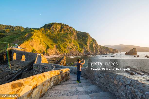 tourist taking a snapshot at sunset at gaztelugatxe, spain - gaztelugatxe fotografías e imágenes de stock