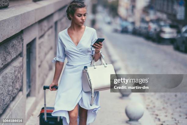 mujer turista con maleta caminando y mensajes de texto en el teléfono - expatriado fotografías e imágenes de stock