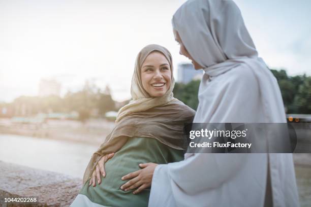 smiling pregnant islamic woman and her close friend - pregnant muslim stock pictures, royalty-free photos & images