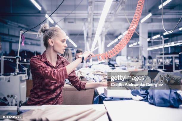 female textile worker blowing the stitching threads from materials - needlecraft product stock pictures, royalty-free photos & images