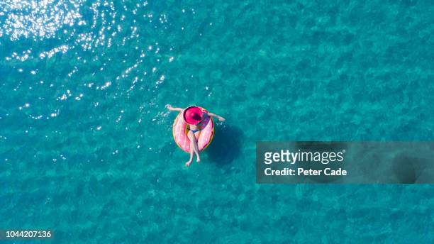 lady floating in the sea in a rubber ring, wearing large hat - schwimmring stock-fotos und bilder