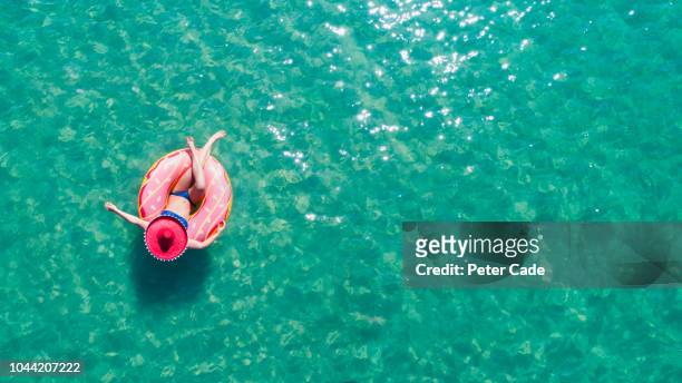 lady floating in the sea in a rubber ring, wearing large hat - beach holiday stock-fotos und bilder