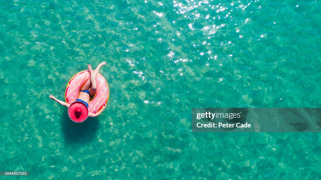 Lady floating in the sea in a rubber ring, wearing large hat