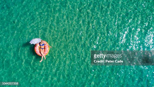 lady floating in the sea in a rubber ring, holding umbrella - sunbathing aerial stock pictures, royalty-free photos & images