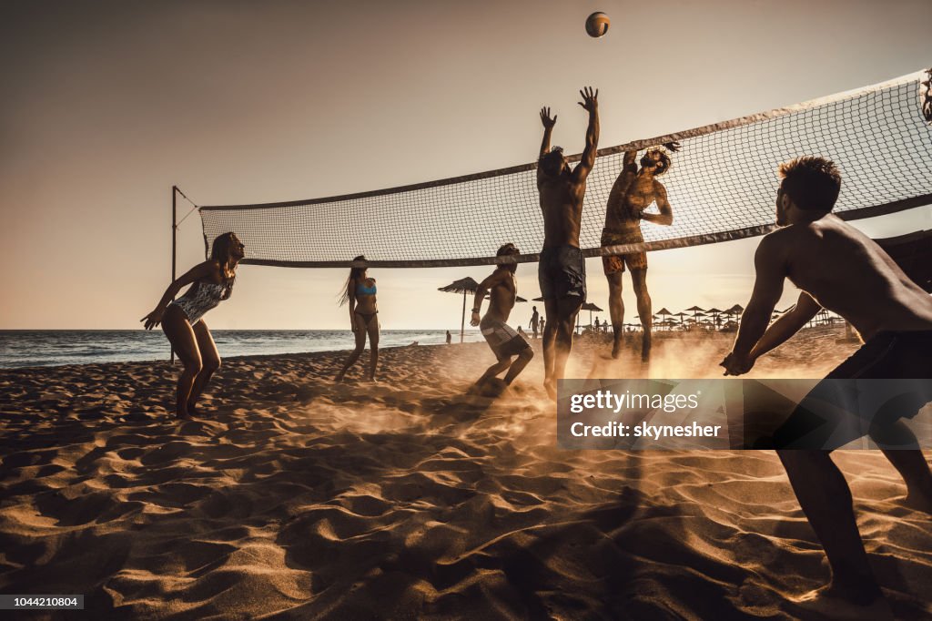 Grande grupo de amigos a jogar vôlei de praia ao pôr do sol.