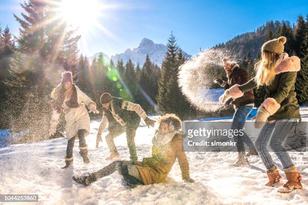 friends having snowball fight out in snow on sunny day - winter vacation stock pictures, royalty-free photos & images