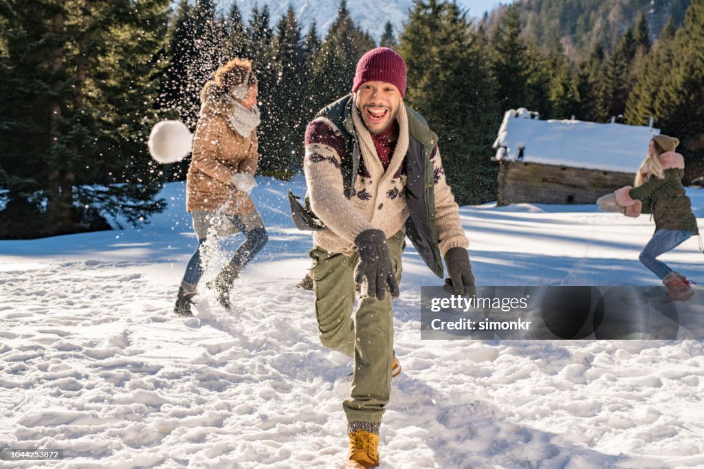 Hombre lanzando bolas de nieve en el aire mientras se divierten con sus amigos