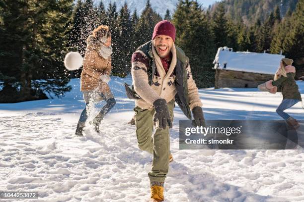 man throwing snowball into air while having fun with his friends - bola de neve imagens e fotografias de stock