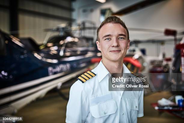 portrait of smiling young pilot in airplane hangar with helicopter - pilota stock-fotos und bilder