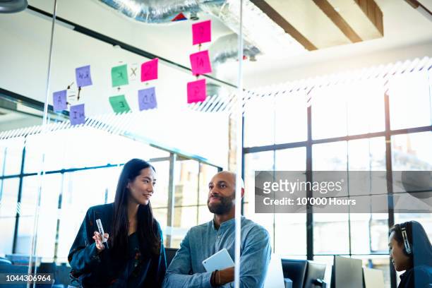 businessman and woman looking at sticky notes on glass - creative director stock pictures, royalty-free photos & images