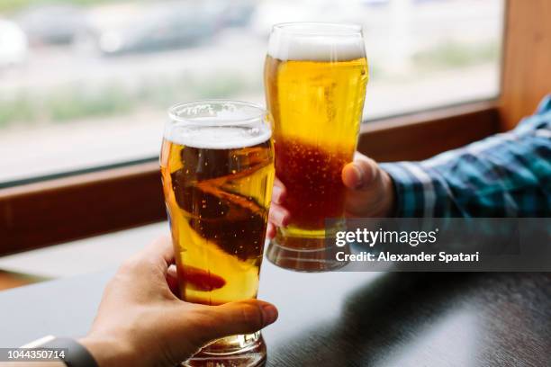 close up of two men's hands holding beer glasses - beer cheers stock-fotos und bilder