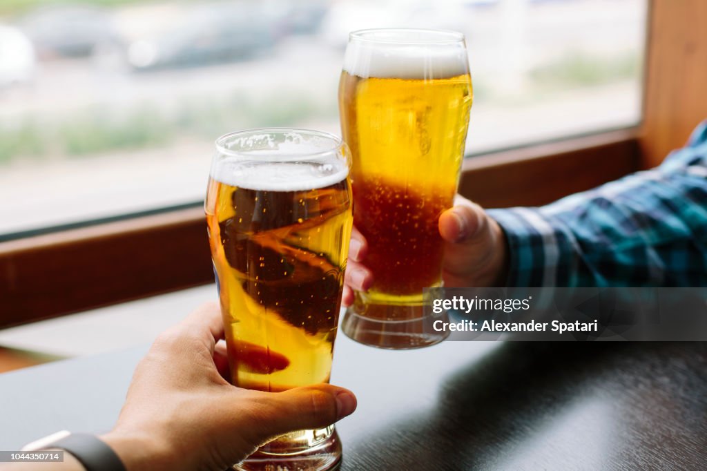 Close up of two men's hands holding beer glasses