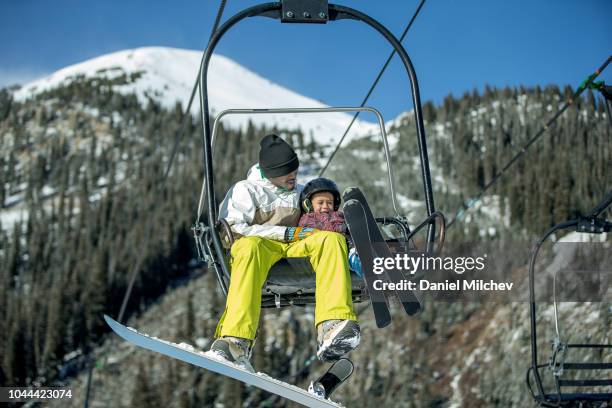 father and son having fun on a chairlift while skiing and snowboarding during the winter at a colorado resort. - keystone stock pictures, royalty-free photos & images