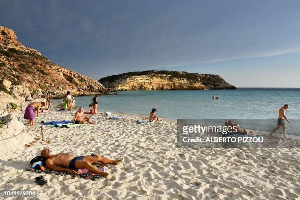 Tourists sunbathe on the beach of the Isola dei Conigli in Lampedusa on September 25, 2018. - Five years after the worst shipwreck of its history,...
