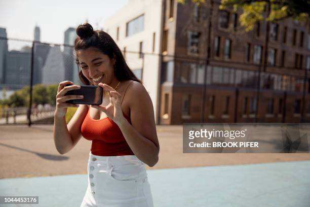 young woman in city taking picture with phone - call us photos et images de collection