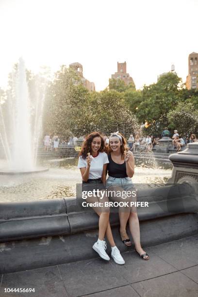 young females hanging out on city park water fountain eating ice cream - freundinnen urlaub sommer eis stock-fotos und bilder