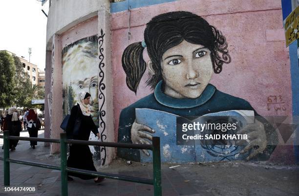 Palestinian woman walks in front a mural painted on a wall of the headquarters of the United Nations Relief and Works Agency in Gaza City on October...
