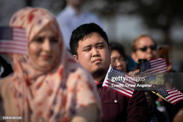 New American citizens wave American flags while 'America The Beautiful' is sung during a naturalization ceremony at Liberty State Park, October 2,...