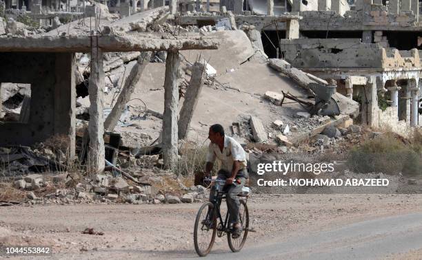 Syrian man rides a bicycle past destroyed buildings in an opposition-held neighbourhood of the southern city of Daraa on October 2, 2018.